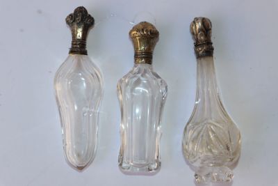 trois bouteilles en verre avec des bouchons dorés et un bouchon doré posé sur une surface blanche