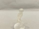 une figurine en verre représentant une femme assise sur une surface blanche