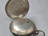 a silver pocket watch with a key in it on a table