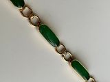 a close up of a green and gold bracelet on a white surface