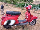 un scooter rouge avec une selle à carreaux, garé dans un champ