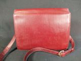 a red leather purse with a long strap on a black background