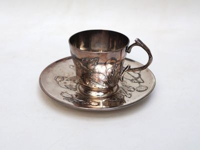a silver cup and saucer sitting on a white table