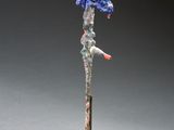 une sculpture représentant un oiseau bleu au bec rouge, posée sur un socle en bois