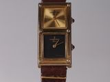 a gold watch with a black face on a display stand