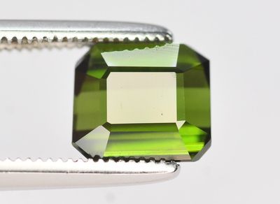 un gros plan sur une tourmaline verte taillée à l'aide d'une pince