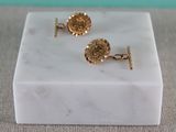 a close up of a pair of gold cufflinks on a marble block