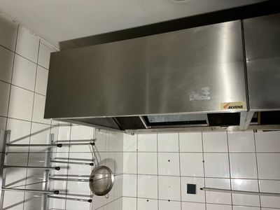 une hotte en acier inoxydable dans une cuisine où une casserole et une poêle sont suspendues au plafond