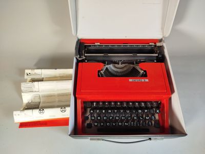 une machine à écrire rouge dans une boîte blanche avec des feuilles de papier