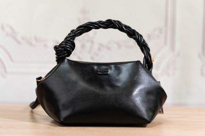 un sac à main en cuir noir muni d'une anse tressée, posé sur une table en bois