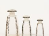 three clear glass bottles with silver trims and lids on a white surface