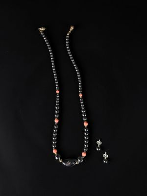 a black beaded necklace with coral and silver beads on a black background