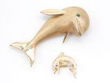 une broche en forme de dauphin en or, avec une pierre verte dans la bouche