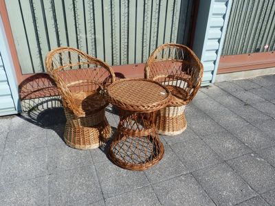 deux chaises en osier et une table sur le trottoir, devant un immeuble