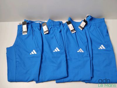quatre paires de pantalons de survêtement Adidas bleus posés sur une table blanche