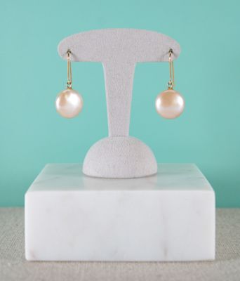 a pair of pearl earrings on a stand against a turquoise background