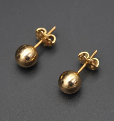 une paire de boucles d'oreilles en forme de boules dorées posées sur une surface noire