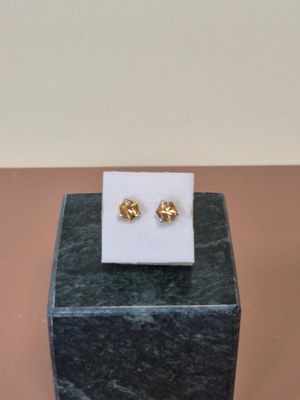 une paire de boucles d’oreilles clous en forme de fleur plaquées or, posées sur un bloc de marbre