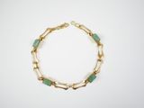 a gold chain bracelet with green glass beads on a white background