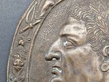 a bronze plaque of a man with a wreath around his neck