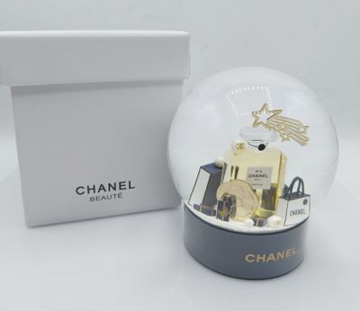 un flacon de parfum Chanel dans une boule à neige, à côté d'une boîte