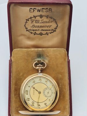 une vieille montre de poche dans une boîte posée sur une surface blanche