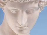 marble bust of a young man with curly hair against a blue background