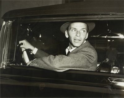 photo en noir et blanc d'un homme assis dans une voiture, la main sur le volant