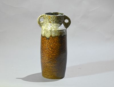 un vase brun et noir posé sur une surface blanche