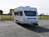 un camping-car blanc garé sur un parking près d'une clôture