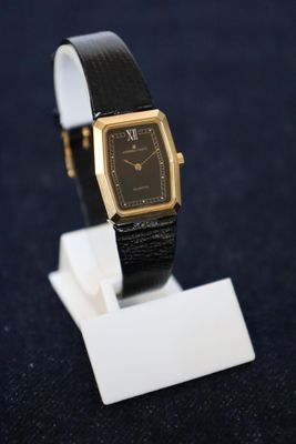 une photo d'une montre noire et dorée posée sur un socle blanc