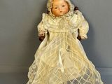une poupée à l'ancienne assise sur une chaise en bois, vêtue d'une robe blanche et d'un bonnet