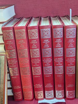 Plusieurs livres rouges sont empilés sur une table rouge, devant un fond rouge.