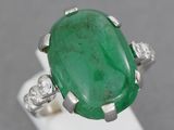 an oval emerald and diamond ring on a white stand
