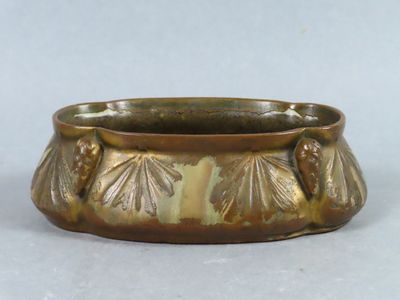 a gold colored bowl with leaves on it on a white surface