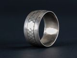 a close up of a hammered silver ring on a black surface