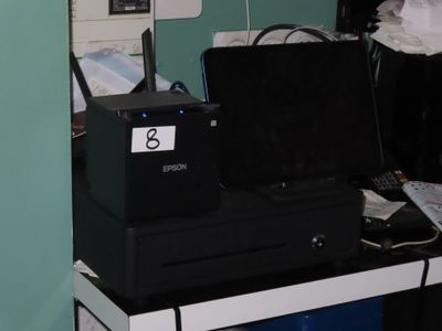 une imprimante noire posée sur un bureau, à côté d'une poubelle bleue