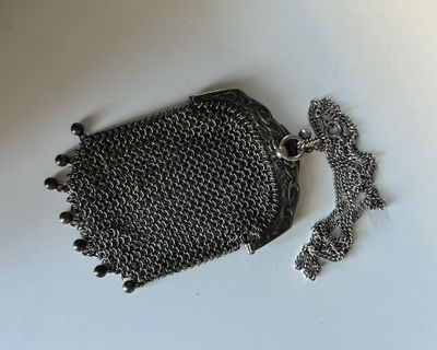 sac à main en cotte de mailles argentée, avec une chaîne et un pompon, sur un fond blanc