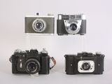 three old cameras sitting side by side on a white surface
