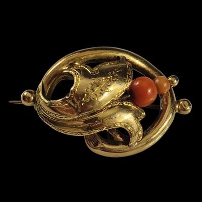 une image représentant une broche en or ornée de perles de corail sur fond noir