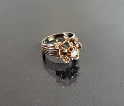 silver and gold ring with a flower design on a black surface