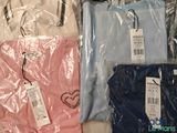 three shirts are wrapped in plastic and one is pink, one is blue and the other is white