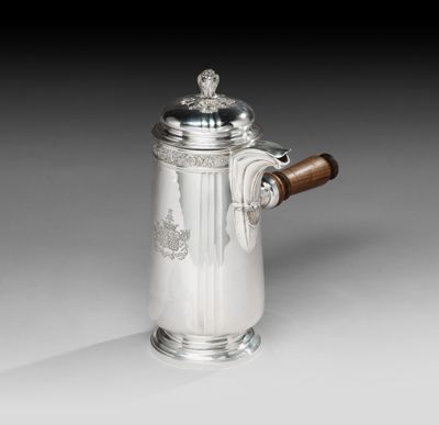une cafetière ancienne en argent, dotée d'une poignée en bois, posée sur un support blanc