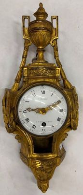 a gold clock hanging on the wall with roman numerals on it
