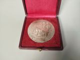 an old silver medal in a red box on a white surface