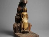 an old wooden statue of a woman sitting on a rock