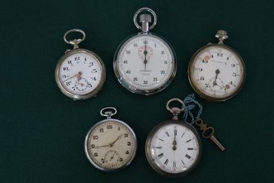 Plusieurs modèles différents de montres de poche sont exposés sur un fond vert