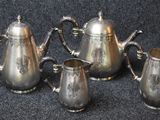 four pieces of silver tea and coffee set on a black surface