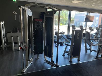 une photo d'une salle de sport équipée d'appareils de musculation et dotée de nombreuses fenêtres