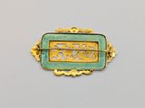 a close up of a gold and green broochle on a white surface